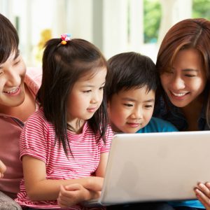 Chinese Family Using Laptop Whilst Relaxing On Sofa At Home